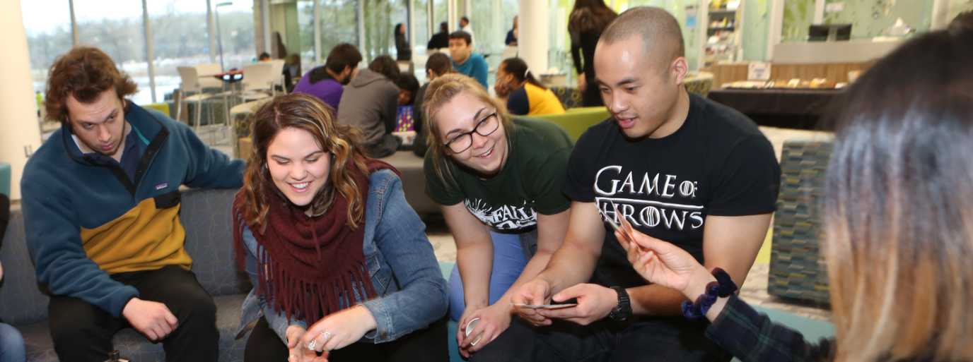 A group of students sit on a couch in the student success area while playing cards.