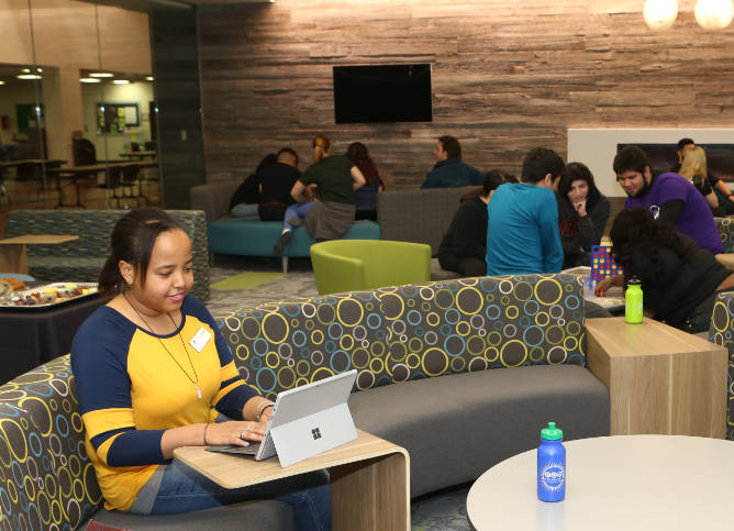 Students sit in the Des Plaines campus lounge. In the foreground is a student using a tablet.