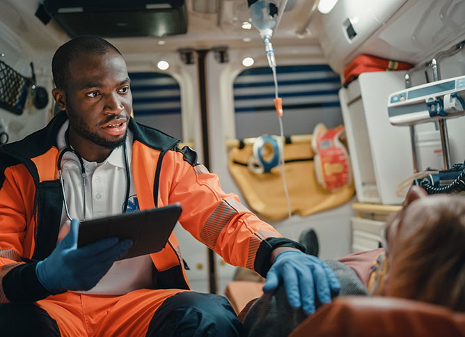 A photo of an African-American Emergency Medical Technician (EMT) in an ambulance with his hand on the shoulder of a patient.