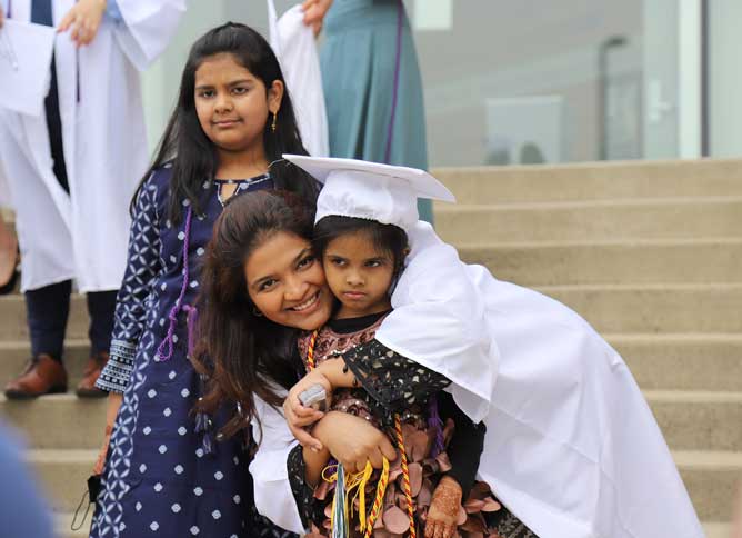 Adult student's child hugging her, wearing cap and gown.
