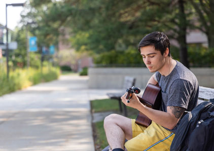 Oakton student playing guitar on outdoor bench.